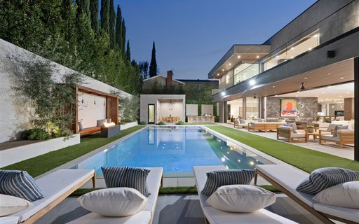 An Indoor pool surrounded by lush greenery, adorned with comfortable chairs and a table, New Construction Home in Tarzana, California