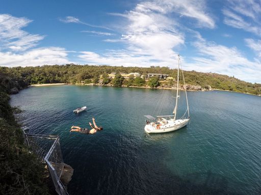A beautiful shot of a sail floating on the body of the water with a person beside jumping into the water