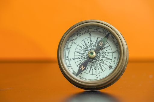 An antique navigational compass with an orange background.
