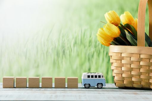 A closeup shot of wooden cubes with a toy bus, and yellow tulips in a straw basket