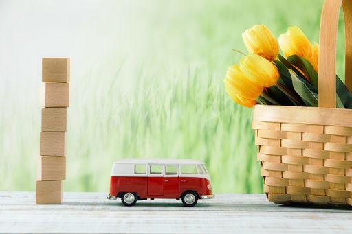 A closeup shot of wooden cubes with a toy bus, and yellow tulips in a straw basket