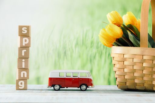 A closeup shot of wooden cubes with "Spring" text, toy bus, and yellow tulips in a straw basket