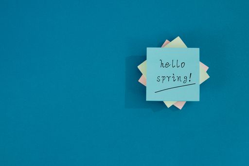 A top view of "Hello spring!" text on a sticker note on a blue background