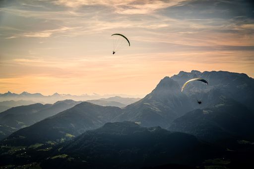 A mesmerizing view of two paragliders flying over the Austrian alps during sunset