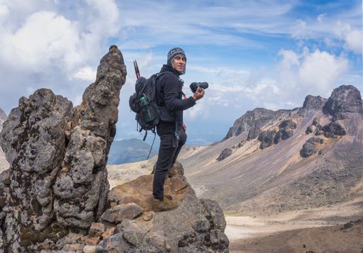 A smiling hispanic hiker with a professional camera on a camera on top of the Iztaccihuatl volcano