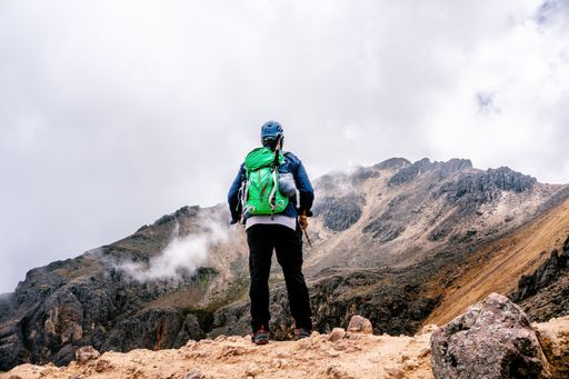 A back view of a hiker with a green backpack observing the beautiful view of the Iztaccihuatl volcano
