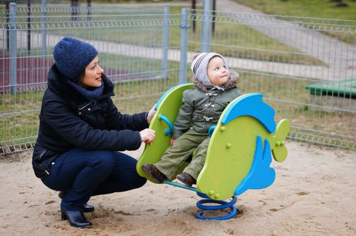 Woman next to a young boy in a swing equipment at a playground.