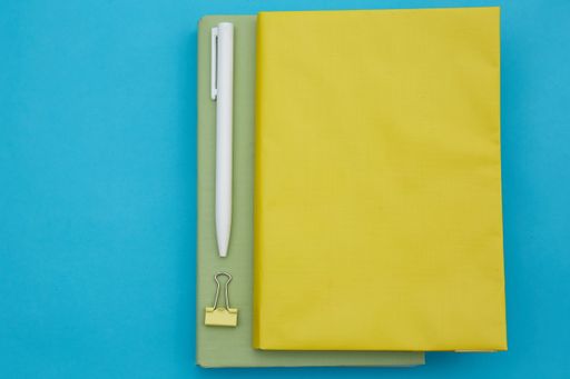 A top view of a notebook, a pen, and a paper clip on a blue background