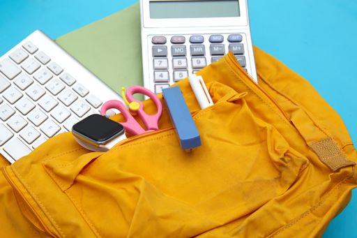 A pen, notepad, and other educational objects on a backpack