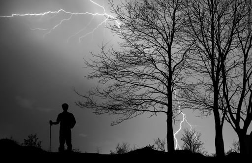A dramatic view of the silhouette of a hiker in a thunderstorm with lightning flashing