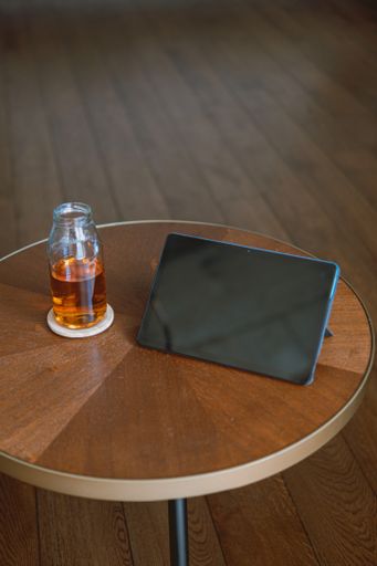 A top view of a black tablet with a blank screen on a wooden round table with a teapot o the side