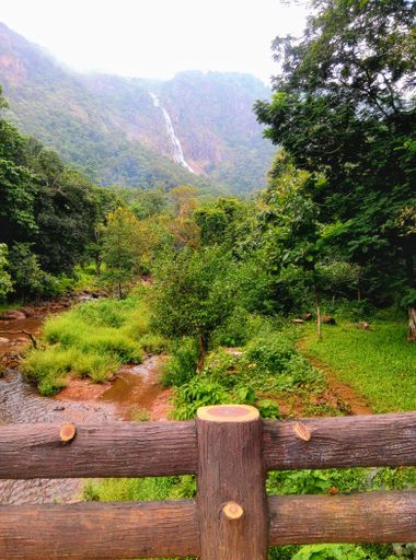 A vertical shot of a wooden fence in the countryside with the Khandadhar Waterfall in the background