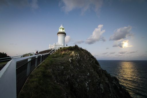 A beautiful shot of a white lighthouse at the top of a hill by the sea under a clear blue sky with white clouds