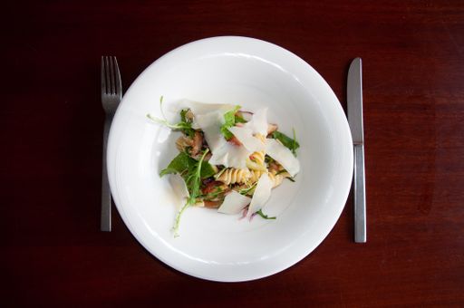 A top view of delicious fusilli pasta with parmesan cheese on a white plant, on a wooden surface with a knife and fork