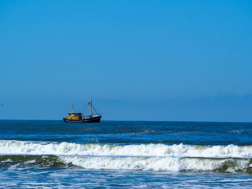 A lone ship sailing on the Wadden Sea in the Netherlands under a clear dark blue sky