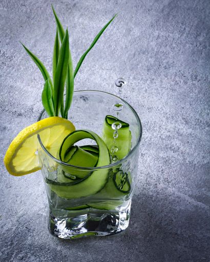 A vertical shot of a refreshing drink with cucumber and lemon slices on a gray surface