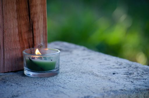 A burning green candle in the small jar put outside on the stone