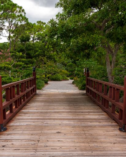 A vertical shot of a wooden bridge leading towards the trees in a beautiful park