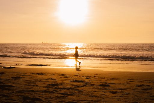 A silhouette shot of a small kid walking along the seashore under the scorching sun