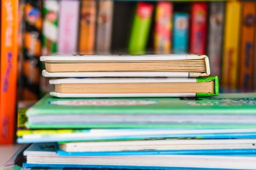 Pile of children books laying on a wooden shelf.