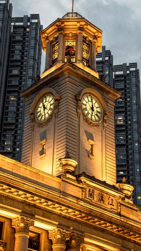 A vertical low angle shot of a city skyline with an illuminated gold clock tower in Wuhan