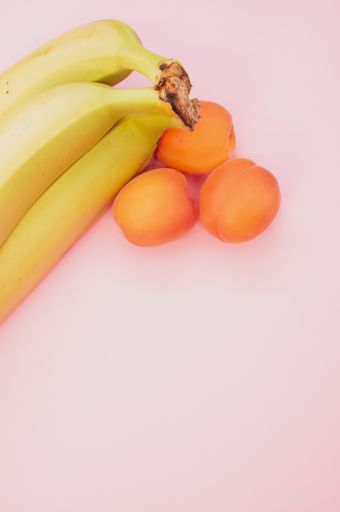 A vertical shot of ripe bananas and apricots isolated on pink background