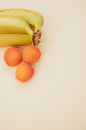A vertical shot of ripe bananas and apricots isolated on light brown background