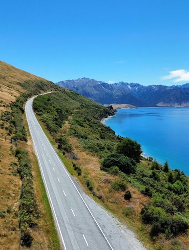 An aerial view of a road on the shore of Lake Hawea surrounded by lush greenery. New Zealand