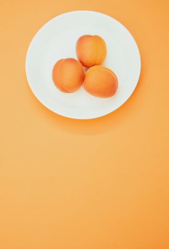 A vertical shot of fresh three apricots on a plate isolated on orange background