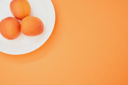A top view of fresh three apricots on a plate isolated on orange background