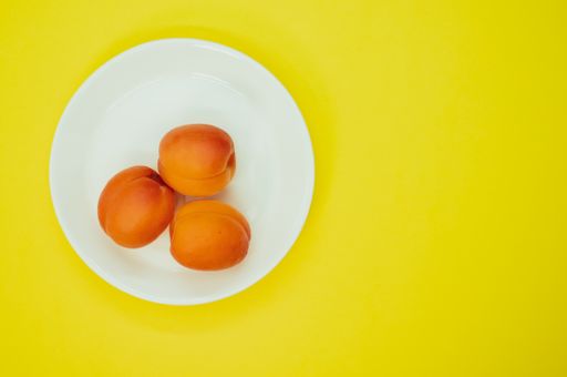 A top view of fresh three apricots on a plate isolated on yellow background