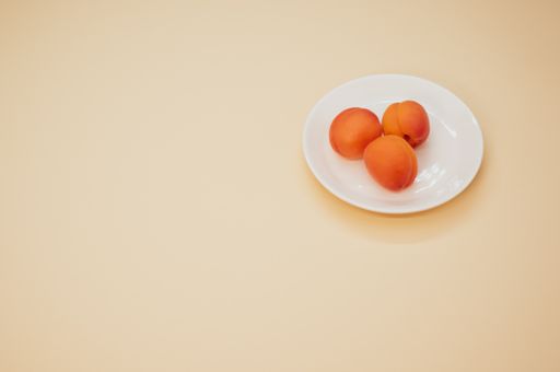 A high angle shot of fresh three apricots on a plate isolated on light brown background