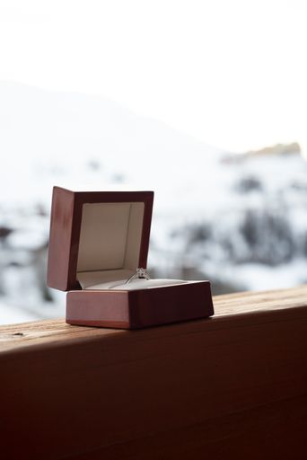 A vertical closeup shot of a wedding ring in a red box on a wooden surface with a blurred background