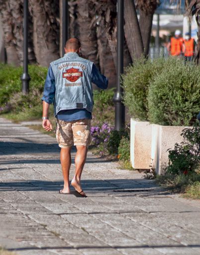 A vertical back view of a male in a summer outfit with a Harley Davidson jean vest