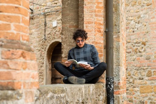 A young Italian man sitting in crossed legs and reading a book