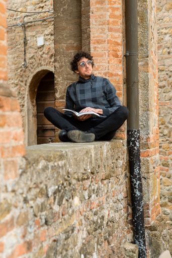 A young Italian man sitting in crossed legs and reading a book