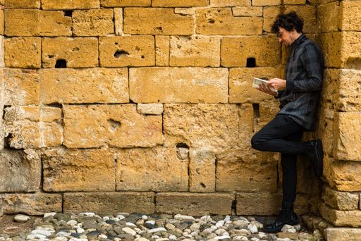 A young Italian man leaning on the wall and reading a book