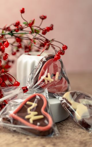 A closeup shot of heart-shaped chocolate candies, adorned with red berries