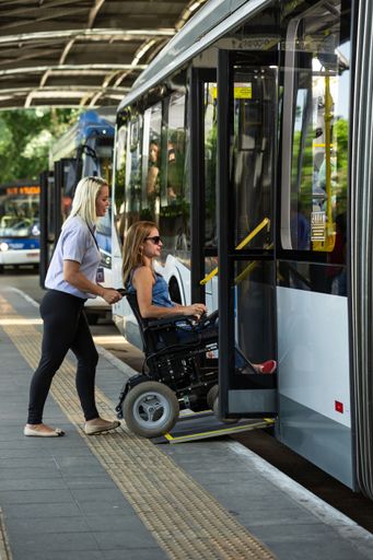 Two women, one an assistant and the other a wheelchair user, getting on the bus via the access ramp