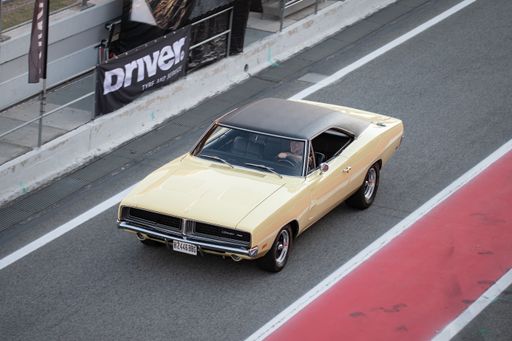 Front view of an impressive 1969 Dodge Charger B-Body American muscle car, it is cream colored and is driving through the pitlane
