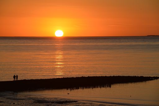 A gorgeous golden sunset over the horizon with the sea reflecting its rays and two people on the shore