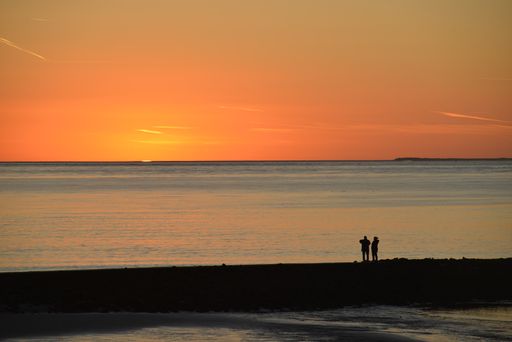 A mesmerizing sunset with golden rays over a clear blue sea and two people standing on the shore