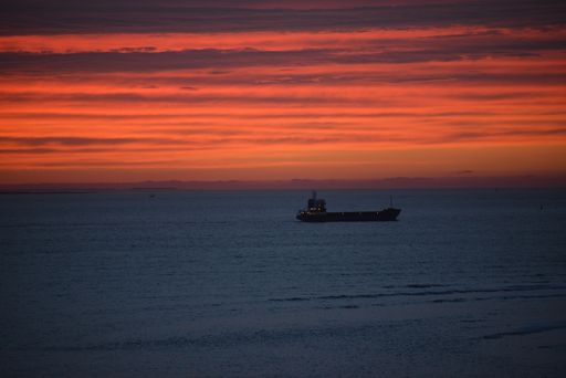 A beautiful golden red sunset shining over the clear blue waters with a boat floating in the middle
