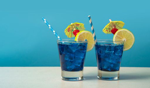 The two glasses of Blue Lagoon cocktail against a blue background