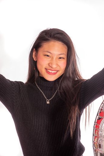 A portrait of a smiling Asian woman in black turtleneck with hands raised with white background
