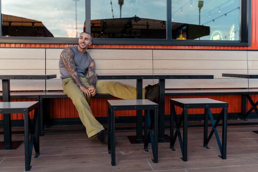 A handsome young man with tattoos, sitting on a bench at an outdoor restaurant