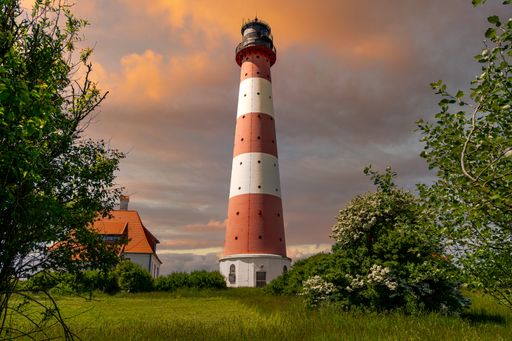 White and orange lighthouse standing in a field surrounded by trees