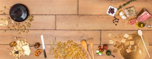 A panoramic shot of assortment on a wooden table: cheese, ham, oil, lard, olives, bread, pasta, wine, grapes, tomatoes, jam, sauces