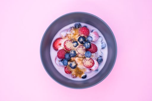 A top view of yogurt with raspberries, blueberries, and powder on a bowl isolated on pink background