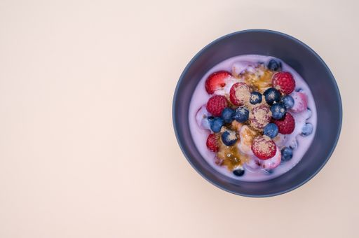 A top view of yogurt with raspberries, blueberries, and powder on bowl isolated on cream background